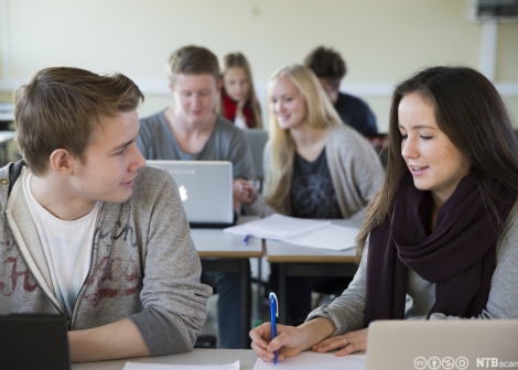 Bildet viser elever i klasserm med pc og skrivesaker foran seg i arbeid, to elever foran er fremhevet